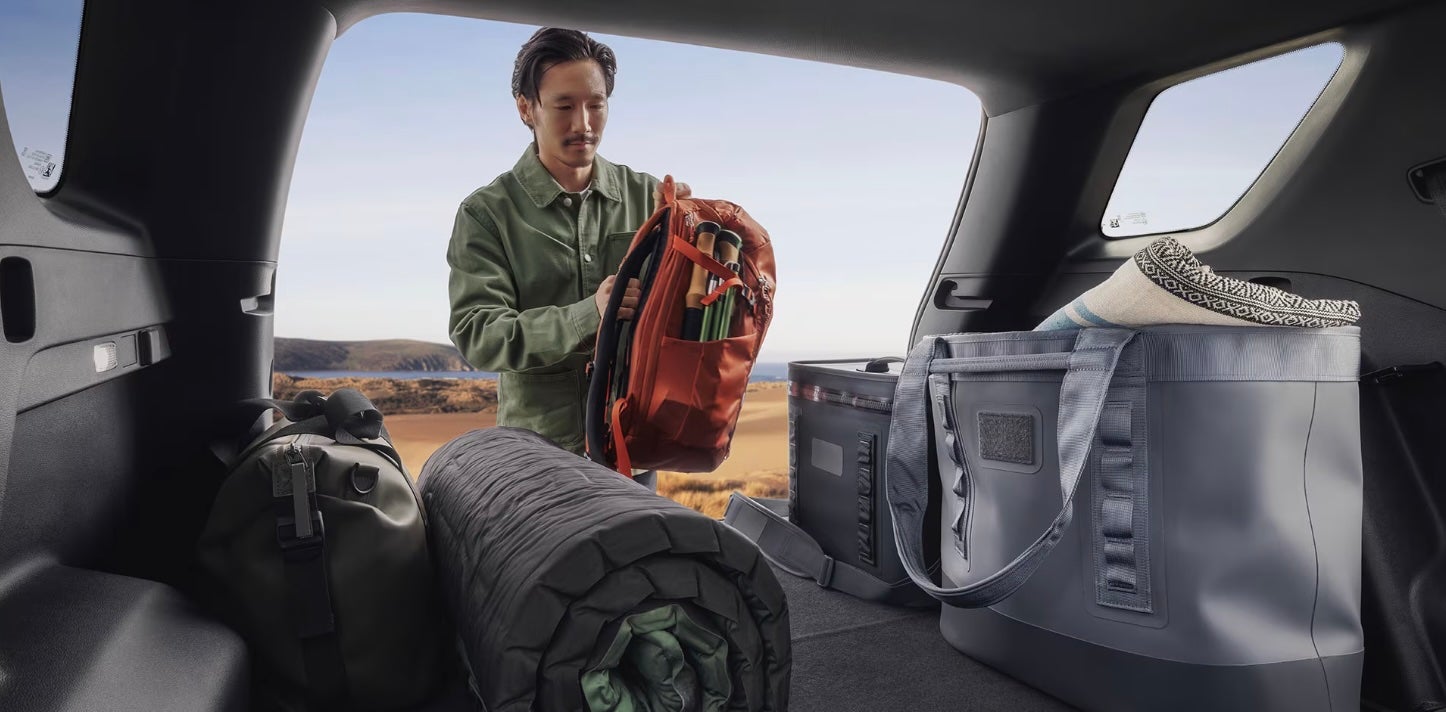 Man putting a backpack in the trunk of a 2026 GMC Terrain.
